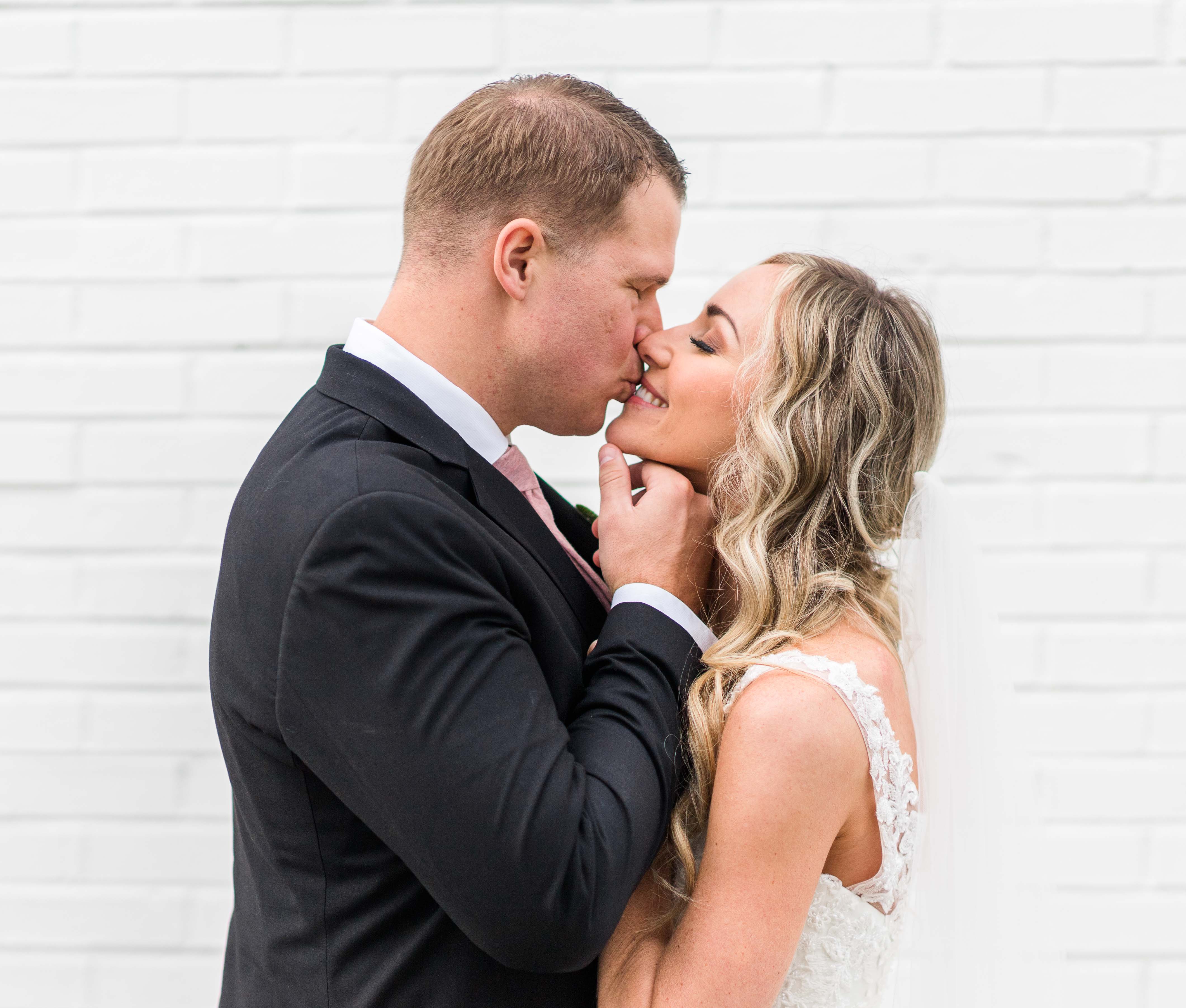bride and groom share a kiss against a white brick wall in charleston