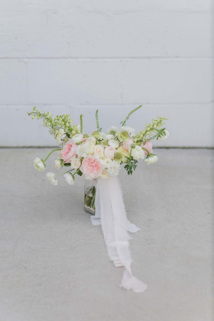 pink, white, and green flowers in a clear vase against a white wall