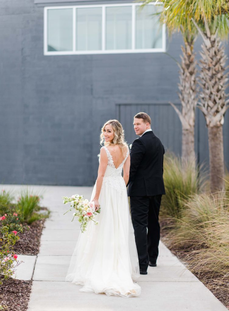 bride and groom walk away towards a blue wall at charleston wedding with palm trees