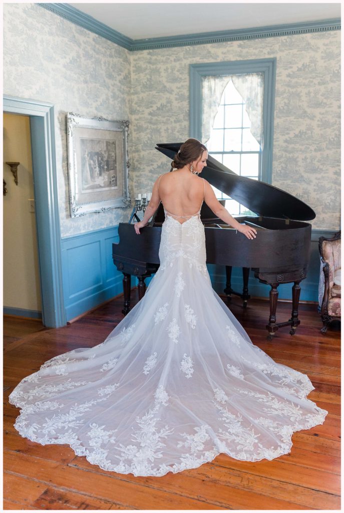 bride with large train stand near piano in vintage looking room