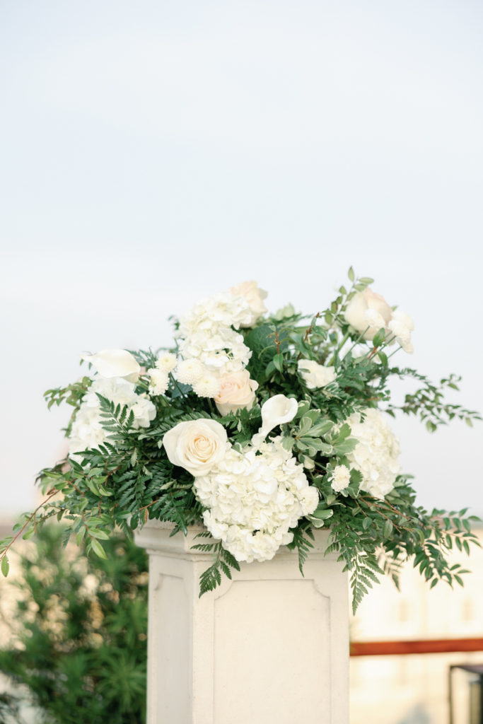 white and green traditional wedding flowers top a white post on luxury wedding rooftop