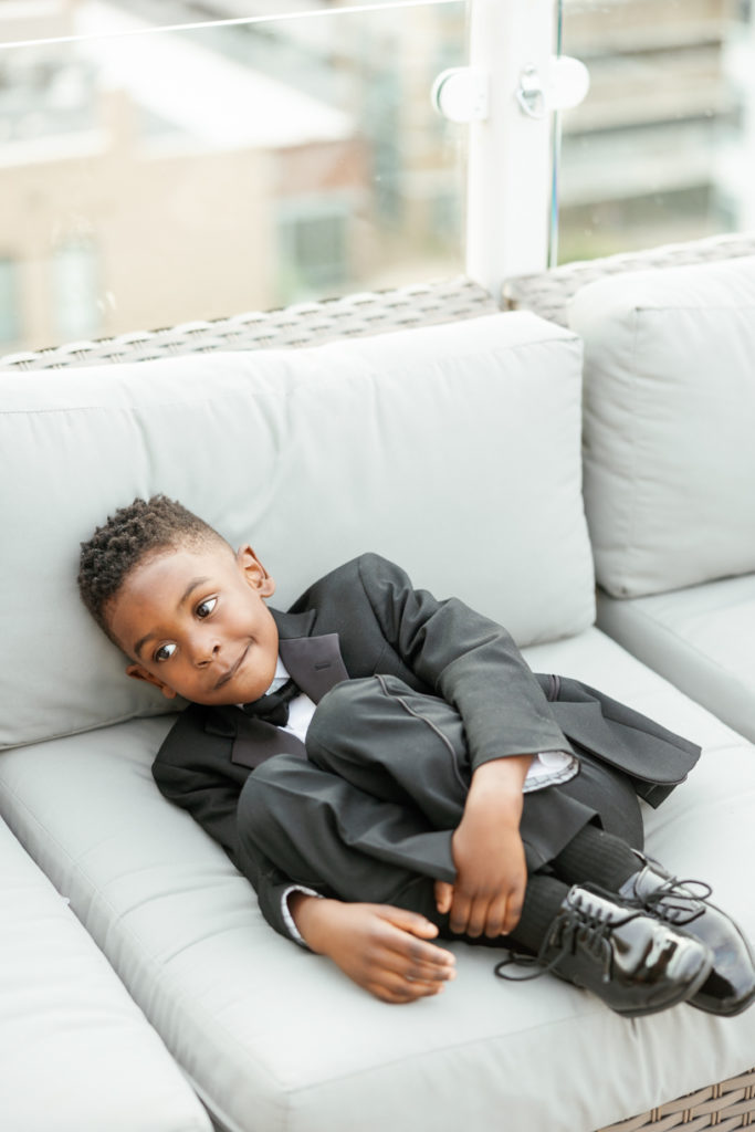 little boy escapes wedding day festivities by laying on a couch in his tiny tuxedo