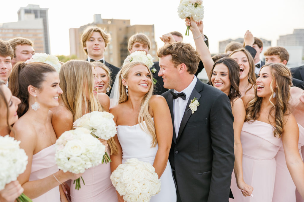 large bridal party in pink dresses and black tuxedos celebrate 