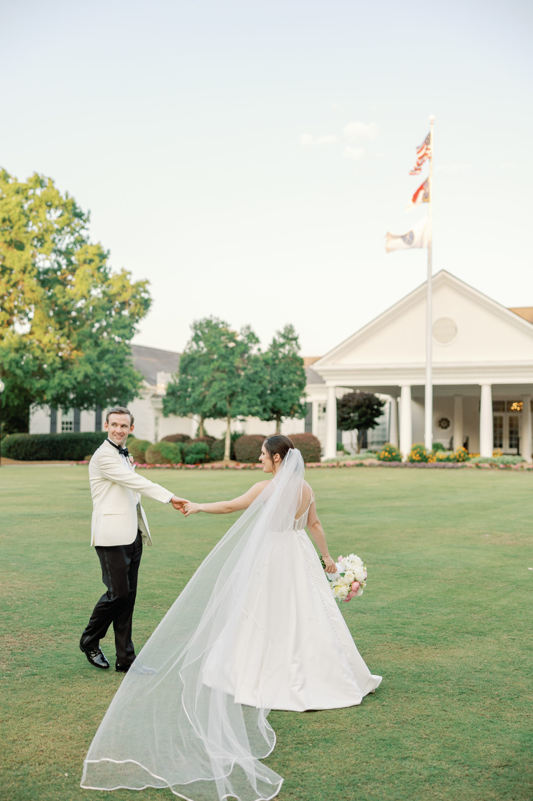 bride with veil and groom with white tuxedo walk towards charlotte country club wedding